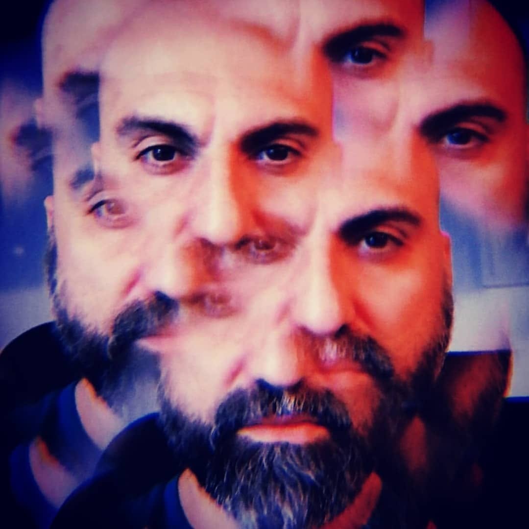 Primer plano de un hombre calvo y con barba, tratado con un efecto de multiexposición o eco que repite su rostro en desplazamiento diagonal, con dominante de color rojiza y azulada.