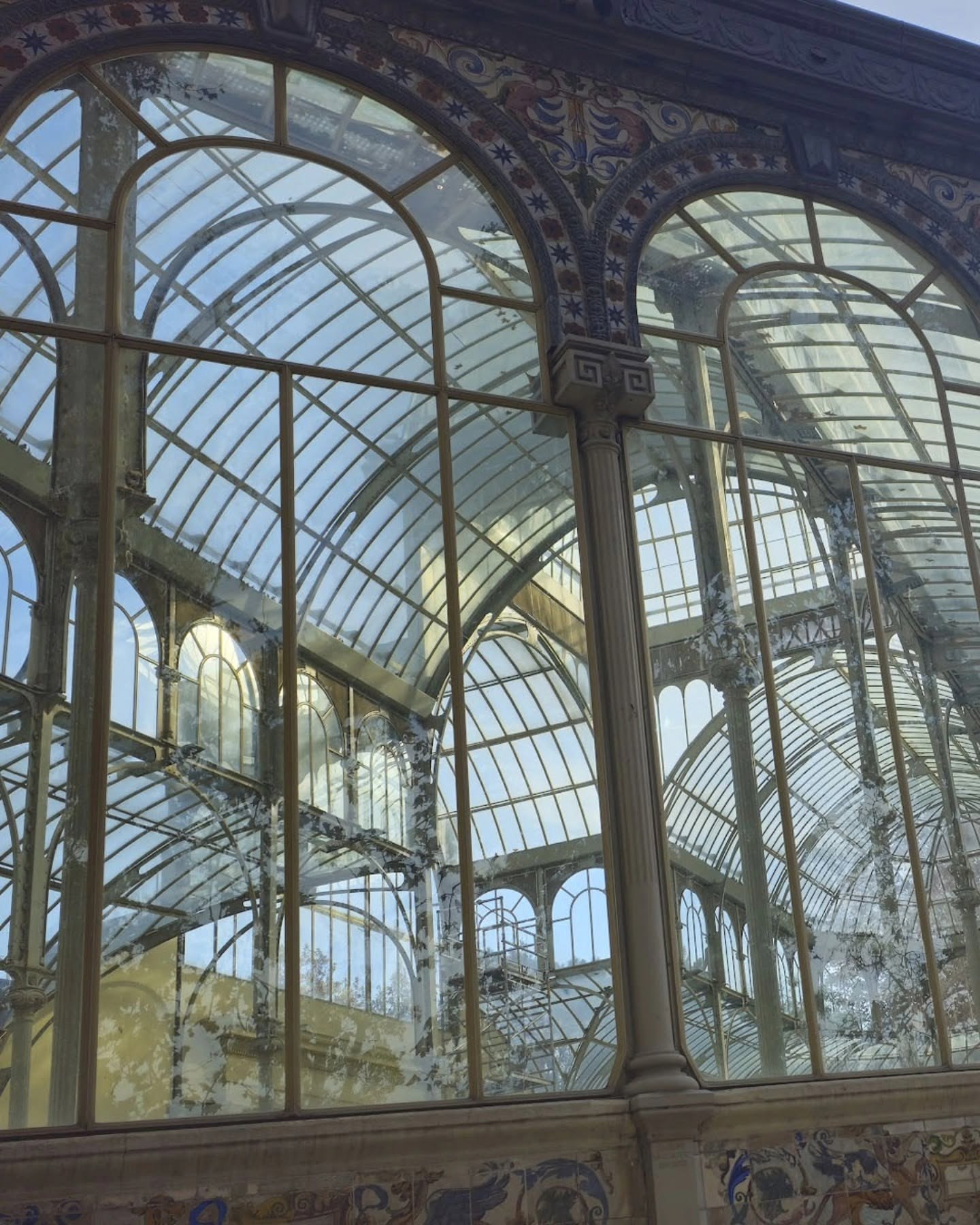 Vista en contrapicado del interior del Palacio de Cristal: arcos metálicos y vidrieras que se repiten en profundidad, con una columna decorada en primer plano.