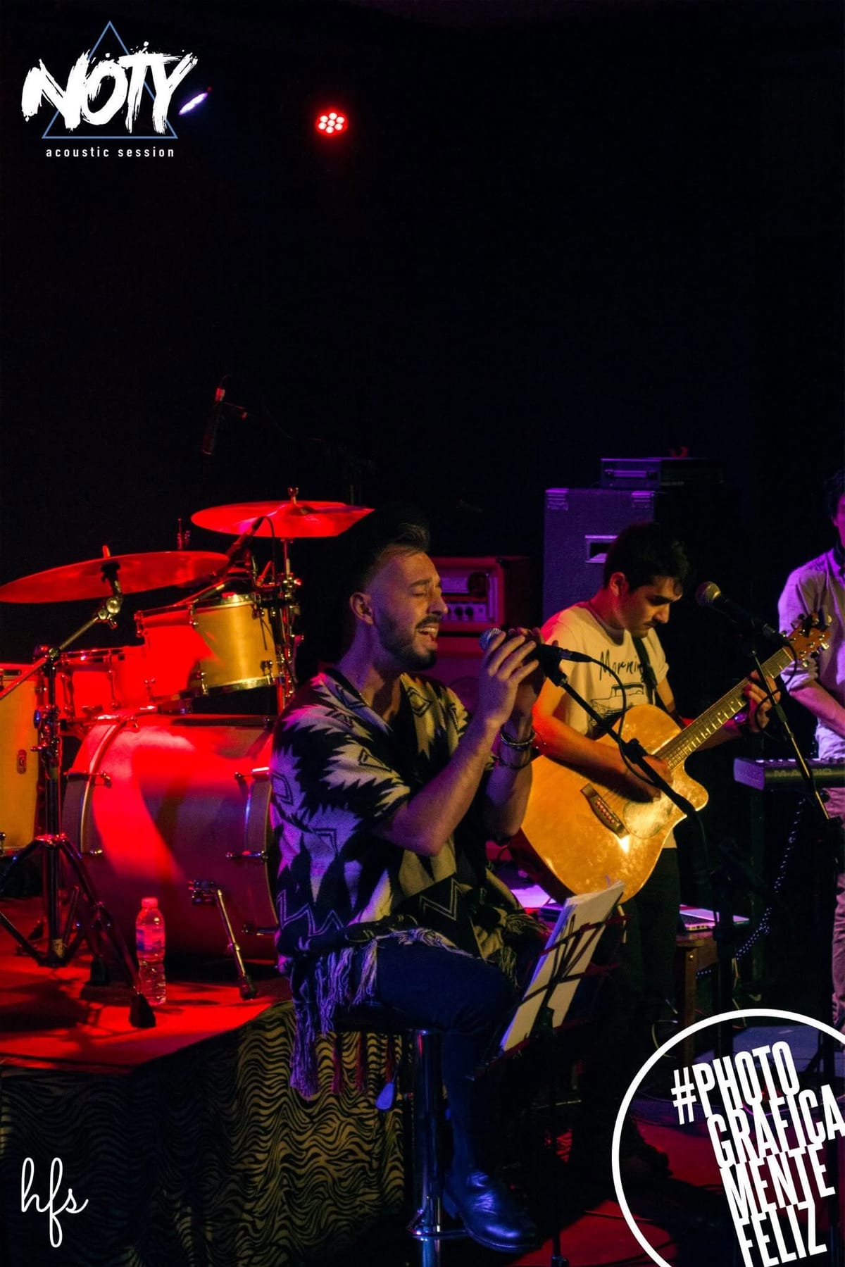 Fotografía a color, con marco blanco tipo póster, del mismo cantante con sombrero y poncho cantando frente a dos micrófonos, bajo luces violeta y celeste; abajo se lee "CANTINA MAK·ENA…