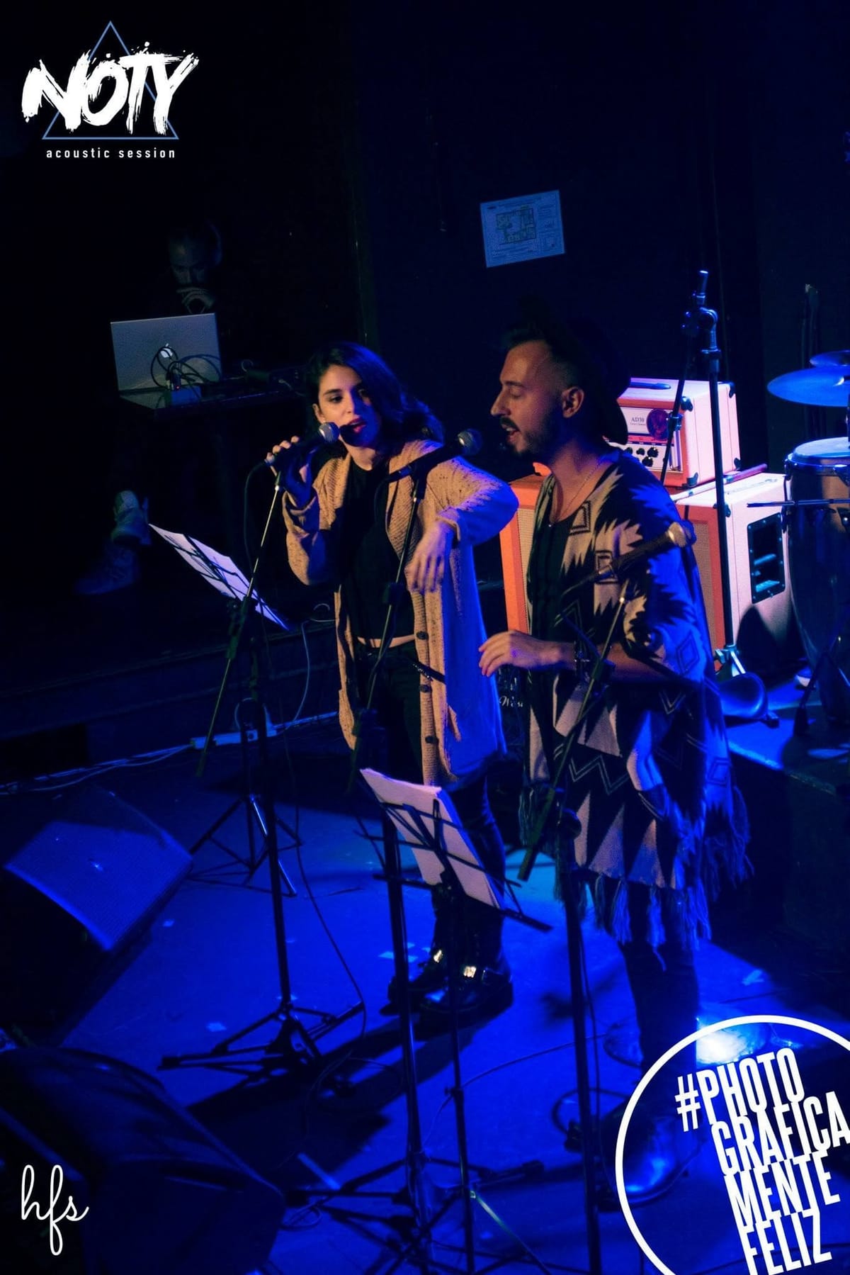 Toma en diagonal y algo elevada de toda la banda en escena: vocalista, guitarrista, tecladista y baterista, cada uno bajo su propio foco de luz azul.