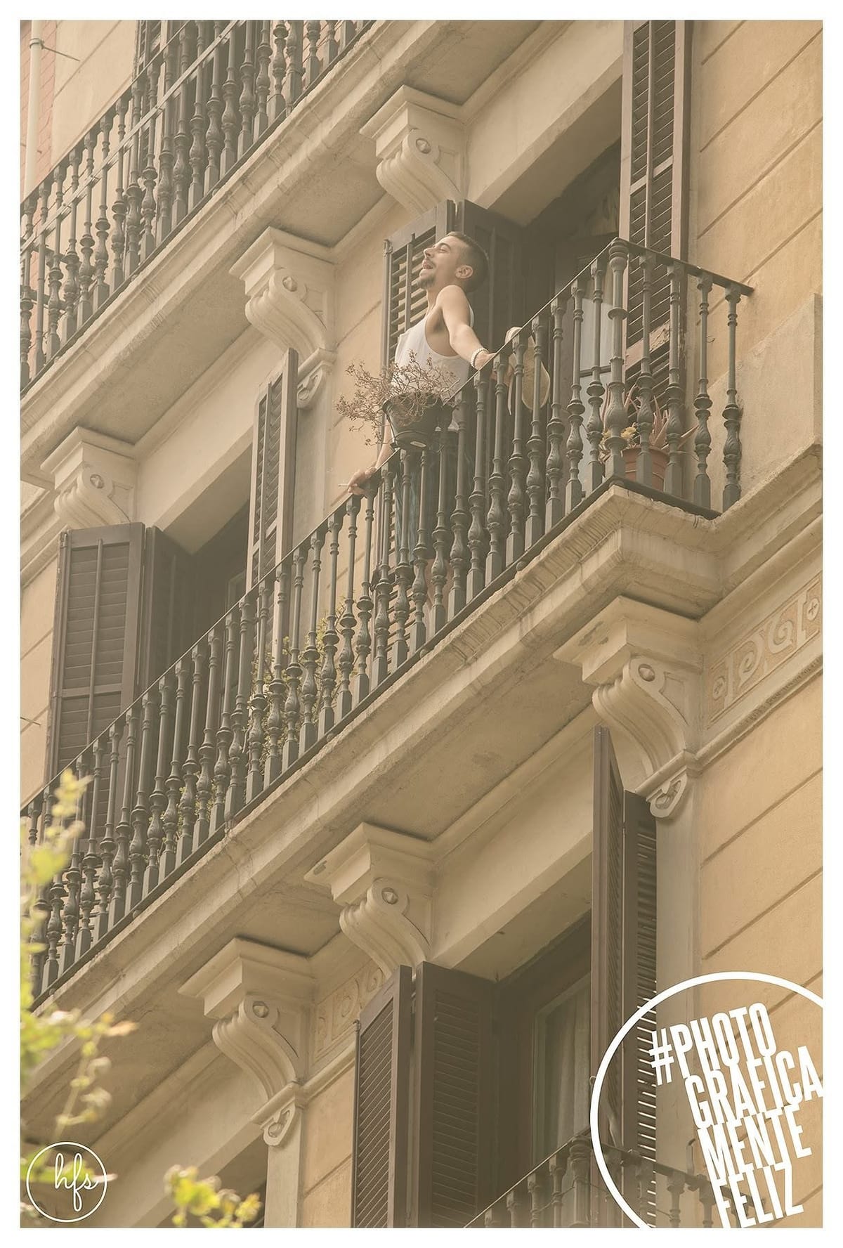 Un hombre joven con musculosa blanca se asoma a un balcón con los brazos extendidos y la cabeza hacia atrás, en un gesto de euforia o canto.