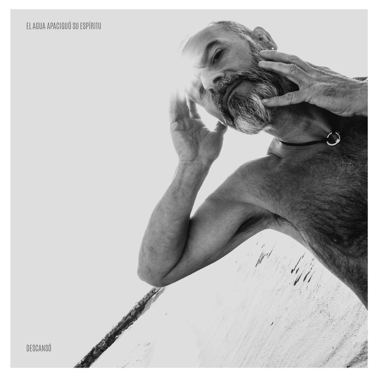 Tercer retrato en blanco y negro del mismo hombre, calvo y con barba, tocándose la cabeza con ambas manos y torso desnudo con vello marcado, fondo muy sobreexpuesto en blanco.