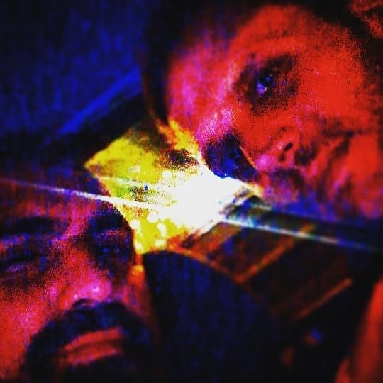 Dos rostros muy cerca de la cámara en una selfie nocturna, con dominante roja y azul intensa y grano visible.