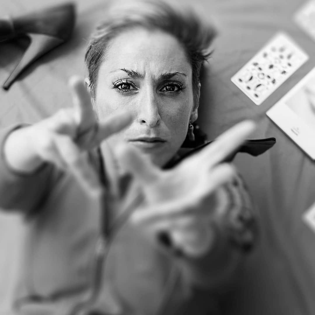 Retrato en blanco y negro tomado desde arriba de una mujer recostada, con las manos extendidas hacia la cámara formando un marco con los dedos.