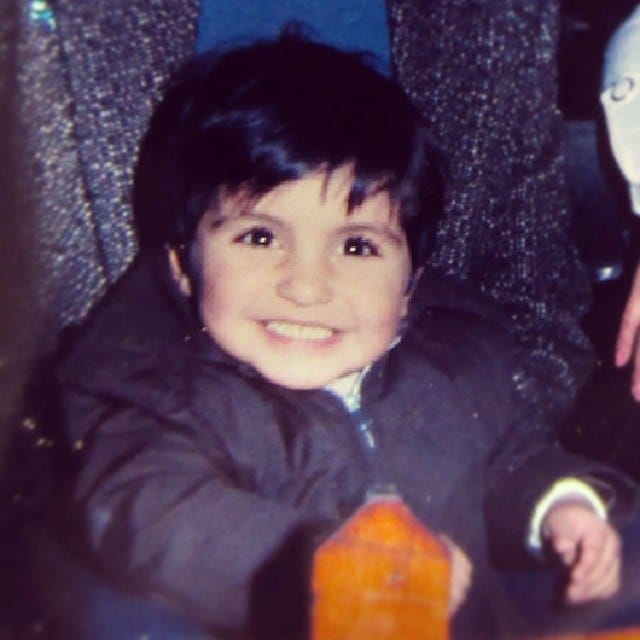 Retrato en primer plano de un nino pequeno de pelo oscuro que sonrie ampliamente hacia la camara, vestido con un abrigo grueso oscuro.