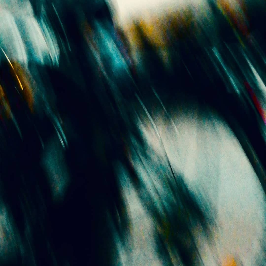 Imagen completamente abstracta dominada por trazos verticales difuminados en tonos verde azulados oscuros que contrastan con zonas claras casi blancas en la esquina superior derecha e…