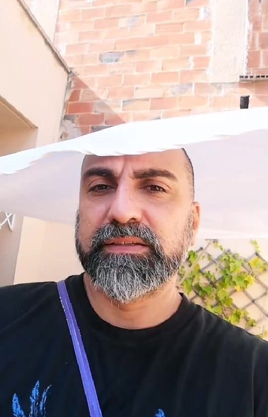 Video casero de una reunión en una terraza soleada: dos mujeres celebran con los brazos en alto junto a un enrejado con plantas, luego un hombre calvo con barba se acerca a la cámara…
