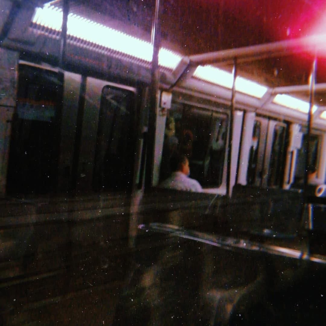 Interior de un vagon de metro fotografiado a traves del vidrio, con fuerte grano y un destello rojo intenso en la esquina superior derecha.
