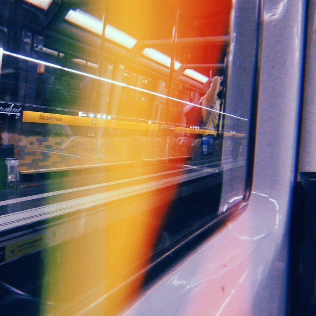 Imagen tomada tambien a traves del vidrio del tren en la estacion Barceloneta, esta vez con fuerte desenfoque de movimiento y bandas de color naranja, rojo y amarillo que atraviesan la…