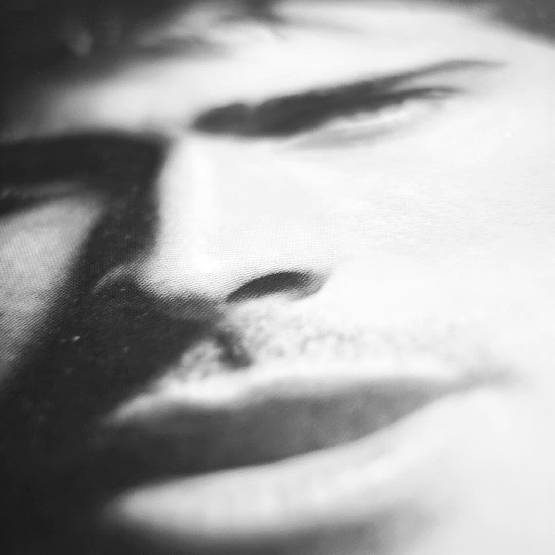 Tercer macro en blanco y negro de un rostro impreso sobre tela, encuadrado de forma aun mas cerrada sobre los ojos, la nariz y la boca, con fuerte grano de trama y contraste marcado entre…