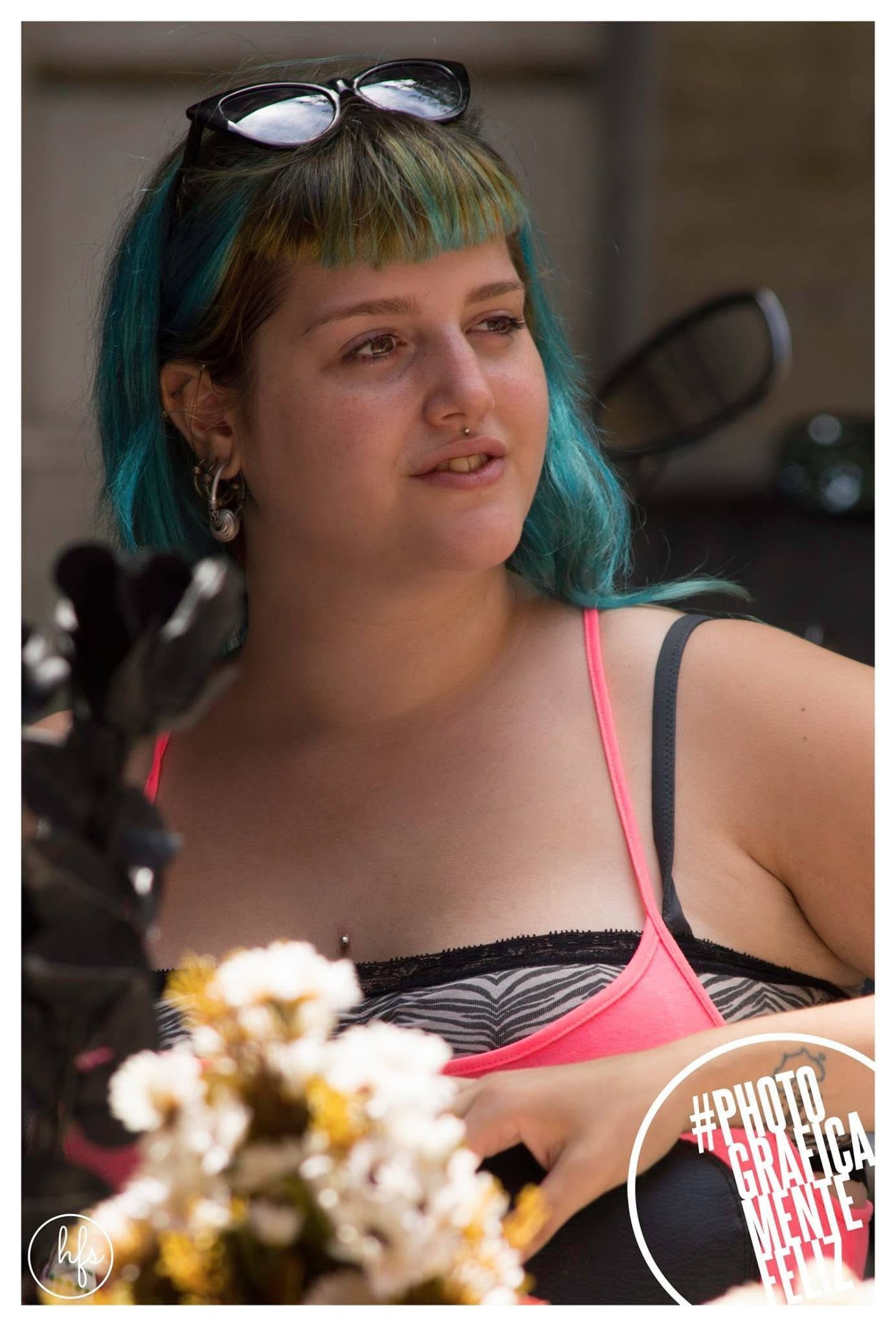 Retrato de una mujer con flequillo corto y pelo teñido en tonos turquesa y verde, anteojos de sol apoyados sobre la cabeza, mirando hacia un costado con expresión relajada.