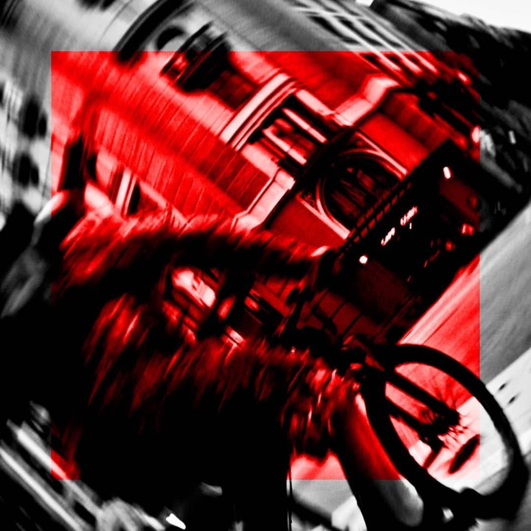 Composicion abstracta en blanco y negro con un recuadro central virado a rojo intenso, donde se distingue borrosamente una fachada urbana y la rueda de una bicicleta en movimiento.