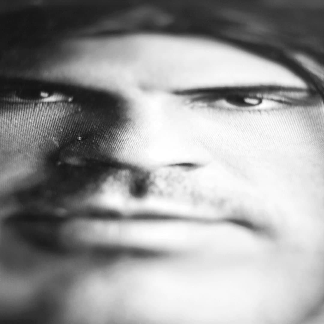 Macro en blanco y negro de un rostro masculino impreso sobre una superficie textil, tan cerca que se aprecia la trama del tejido y el punto de impresion.